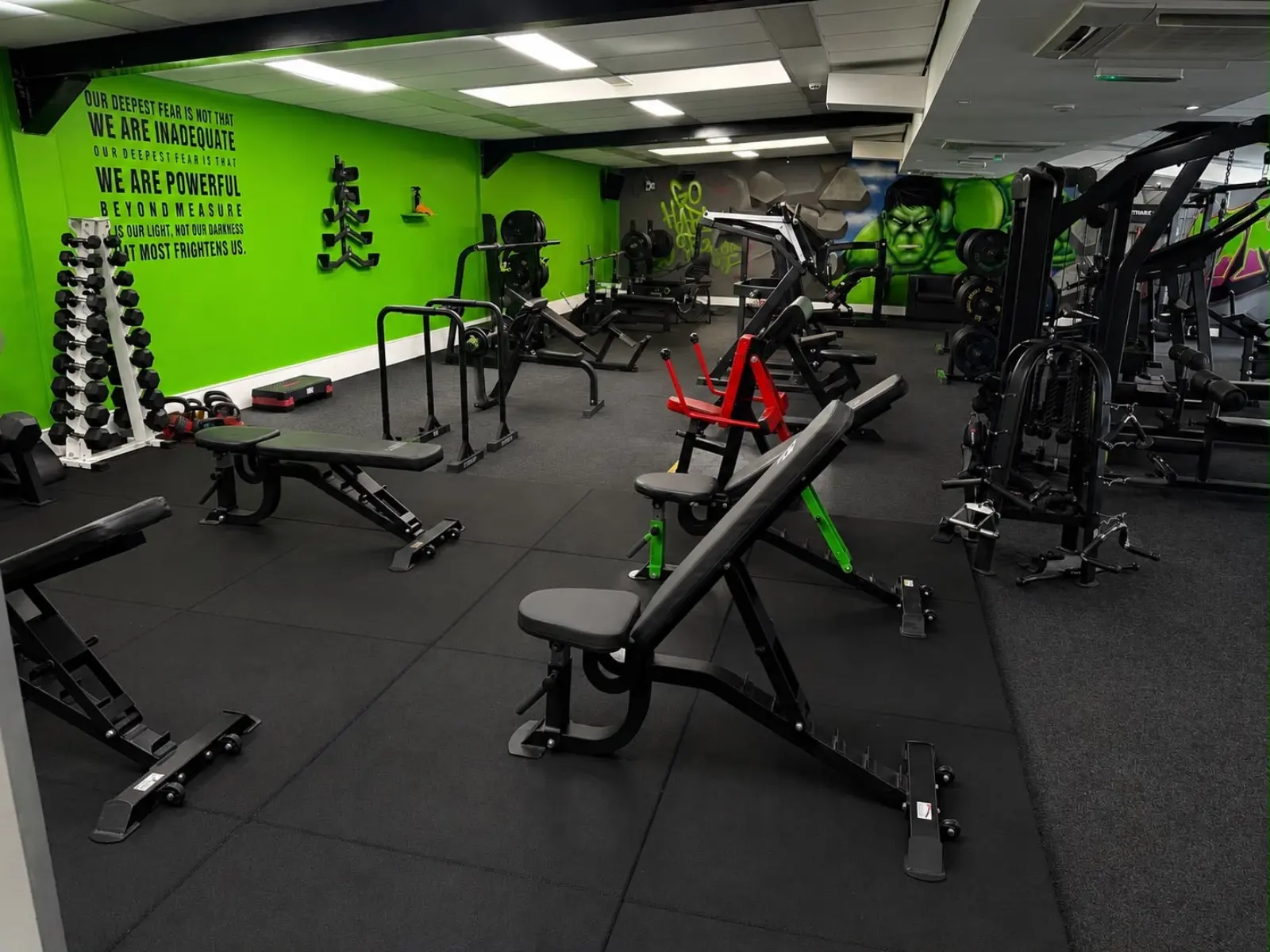 Free weights area with dumbbell racks, adjustable benches and motivational wall mural